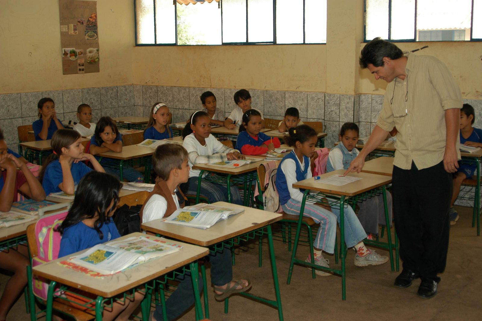 Alunos lendo o capítulo do dia em suas carteiras, acompanhados pelo autor do programa