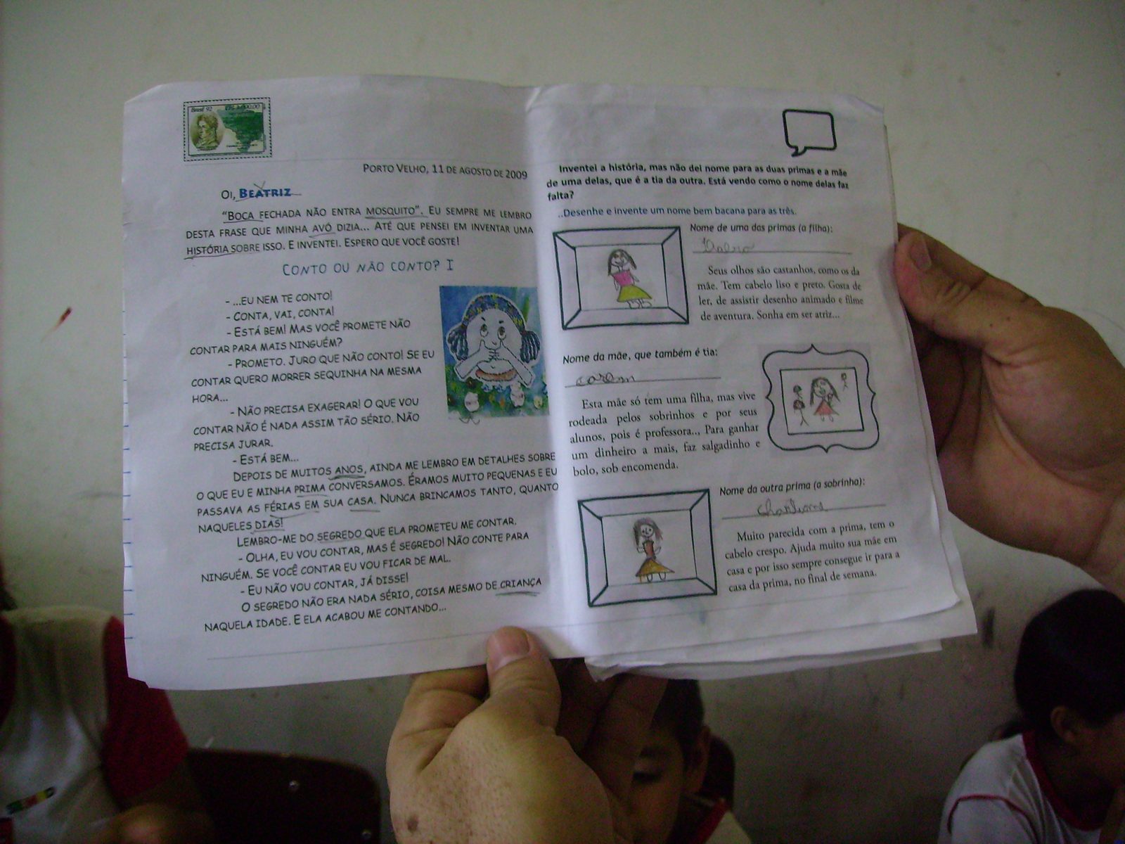 Mãos segurando a folha aberta do material do aluno, com texto e ilustrações